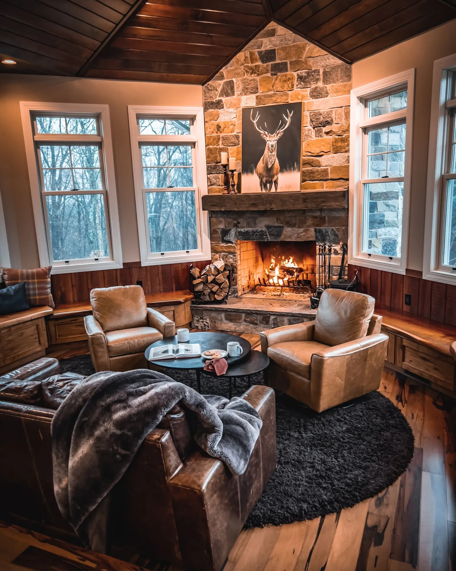 Lodge-style living room with leather chairs around a lit stone fireplace