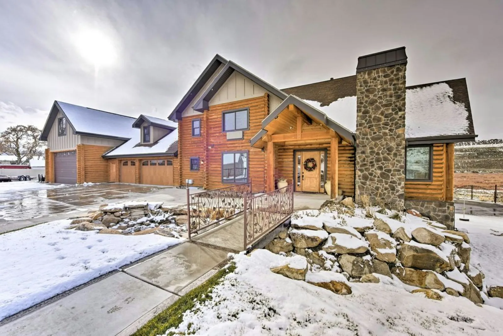 Log home with a tall stone chimney, light snow and a rock garden