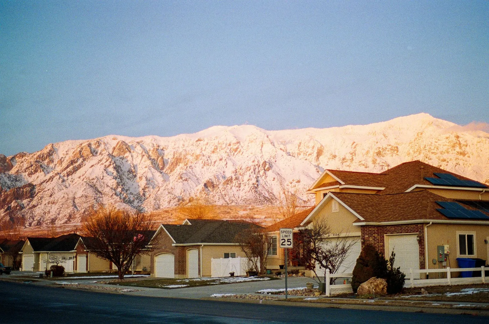 Suburban two-story homes at sunrise below a snow-covered mountain range